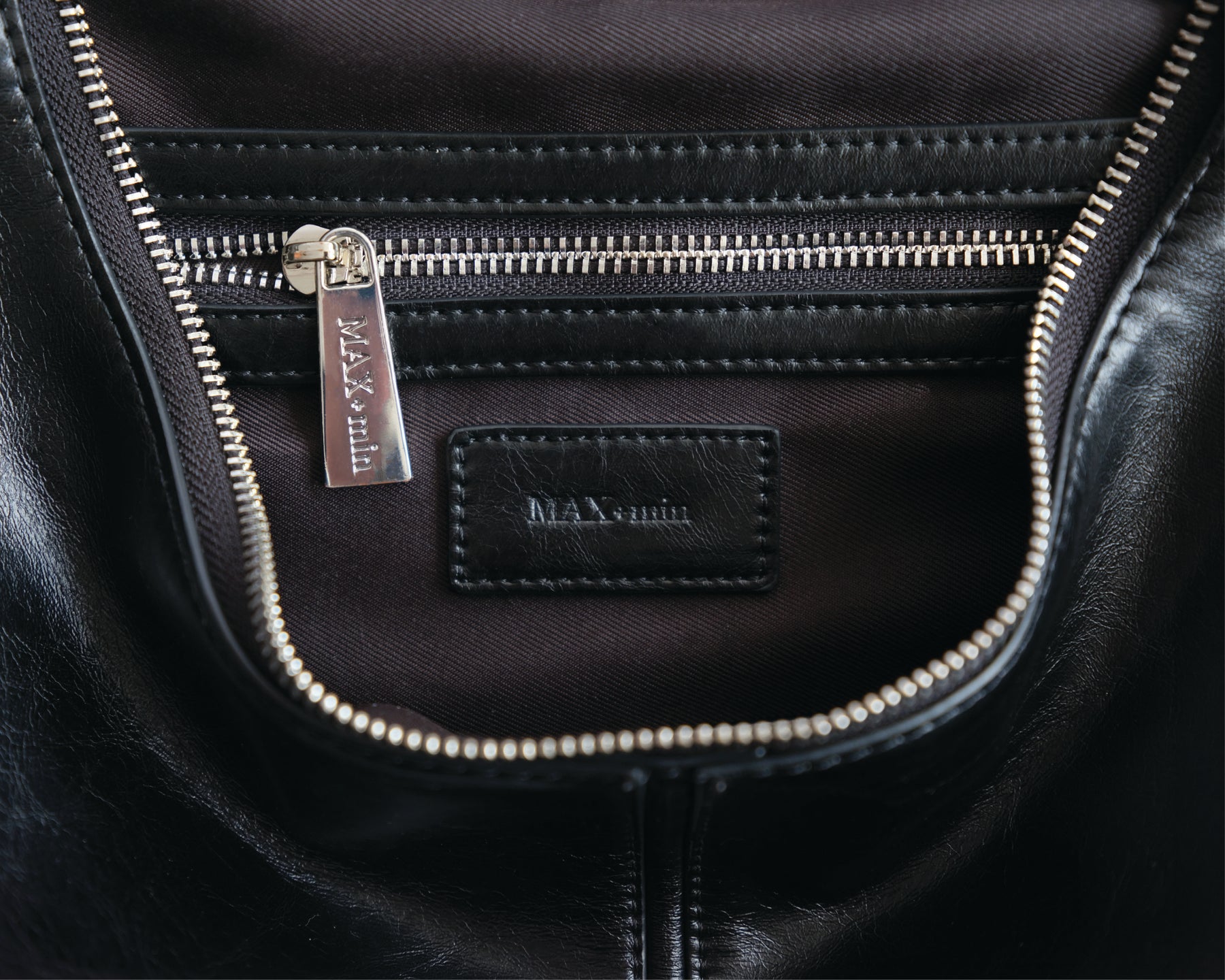 Interior of the MAX+min Maximum Bag showing the zip pocket, black leather lining, and silver-tone hardware.